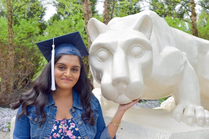 female student in cap and gown at Nittany Lion shrine