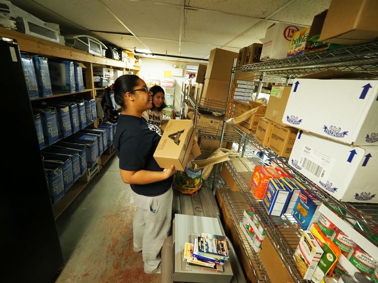 Young woman sorting donations and stacking boxes on shelf