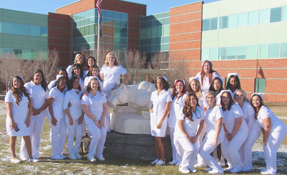 more than 20 women in white nursing outfits posing by Nittany Lion shrine statue