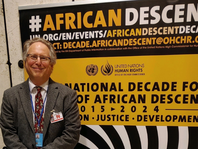 David Livert stands in front of a sign at the Permanent Forum of People of African Descent in Geneva
