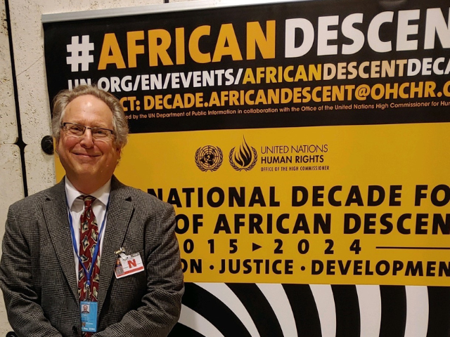 David Livert stands in front of a sign at the Permanent Forum of People of African Descent in Geneva  