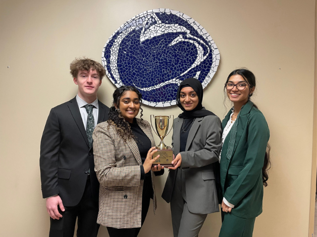 Students holding trophy in front of lion mosaic 