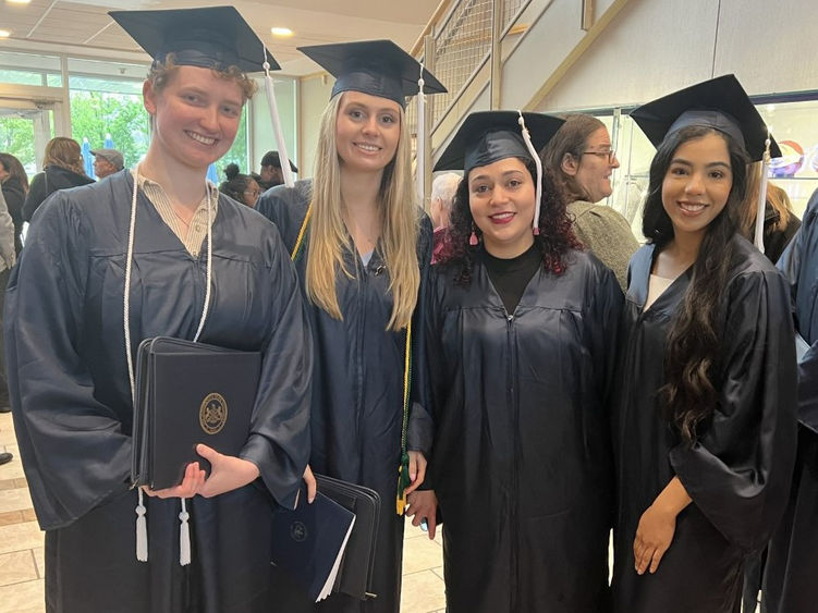 Four graduates wearing caps and gowns pose for picture at a graduation ceremony