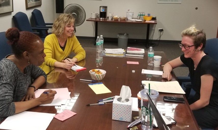 three women at a table smiling while reviewing papers