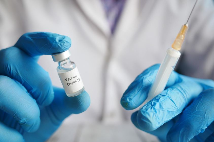 A person wearing blue gloves holding a COVID-19 vaccine vial and a syringe