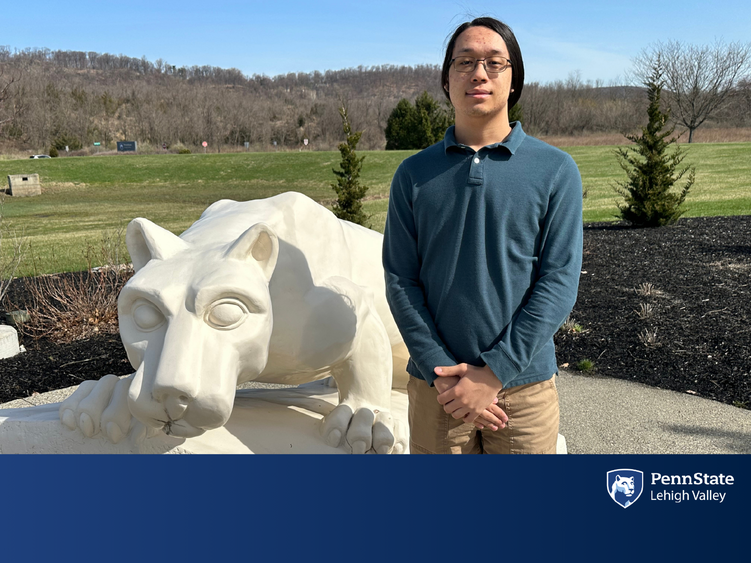 a male college student stands in front of the penn state lion shrine