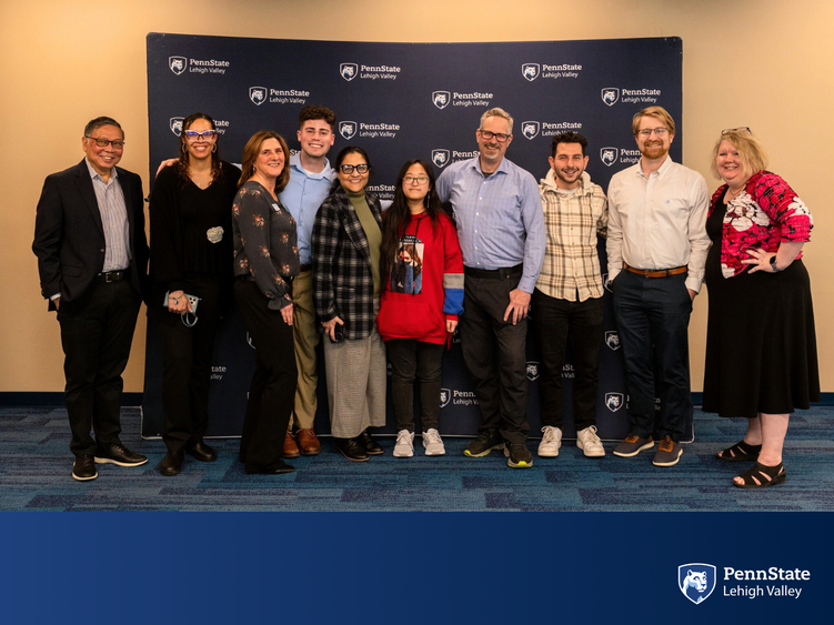 a group of faculty and staff smile in front of a Penn State backdrop