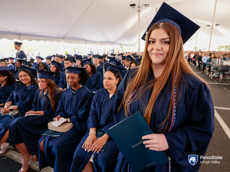 A woman in blue regalia smiles as she holds her blue Penn State Lehigh Valley diploma